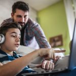 Smiling father and son using digital gadgets in living room