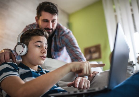 Smiling father and son using digital gadgets in living room